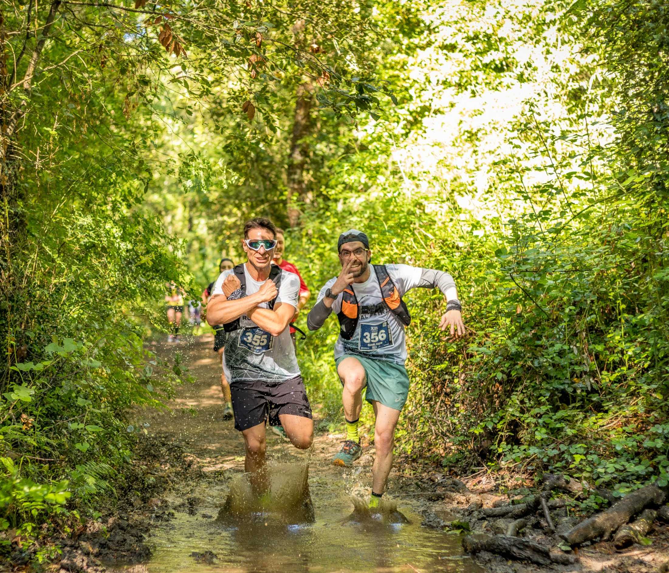 Pareja de corredores saltando por un charco en el bosque de Vallgorguina